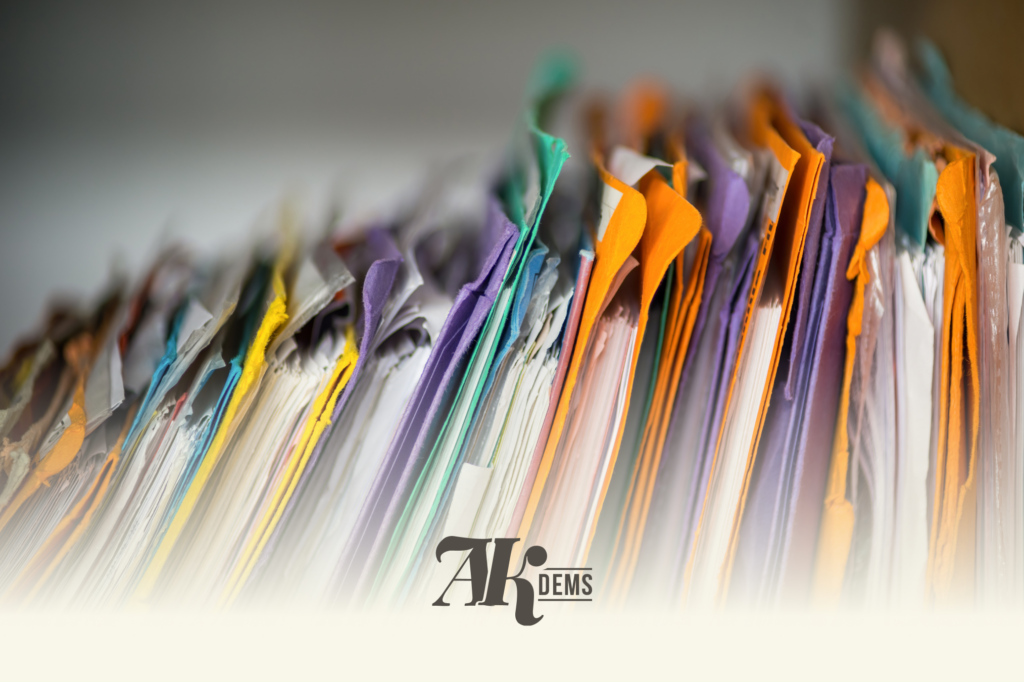 Colorful stack of paper folders with colored tabs, forming a curved row, with AK Dems logo at the bottom.