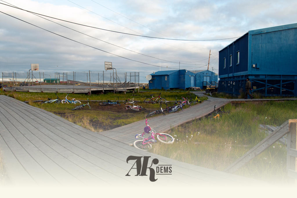 Blue corrugated buildings beside a wooden boardwalk, with scattered children's bikes and a chain-link fence nearby. (informative)