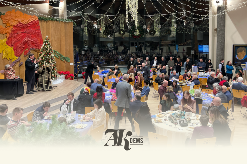 Formal banquet scene with a speaker at a podium, Christmas tree, and guests seated at round tables under string lights.