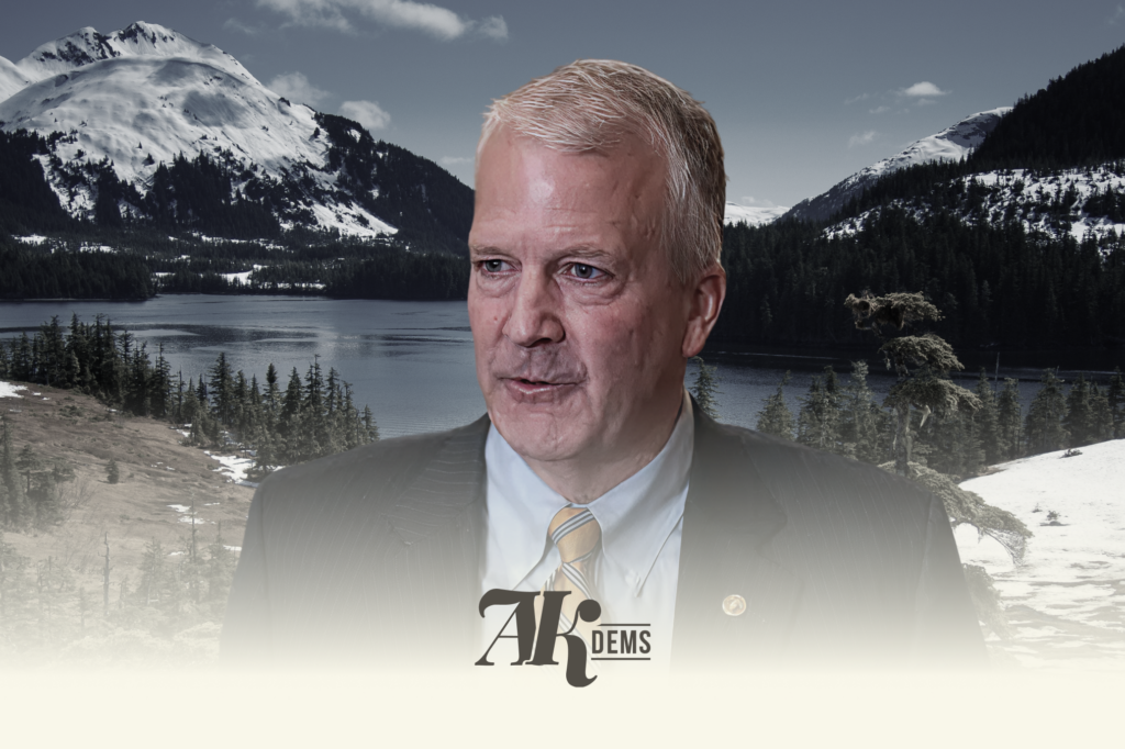 Political campaign banner showing a suited man overlaid on a snowy Alaskan mountain landscape with an AK DEMS logo at the bottom.