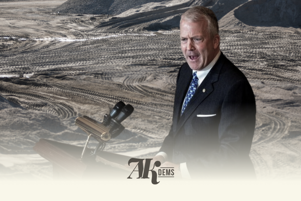 Man in a dark suit and blue tie speaks in a barren desert, with equipment on a tripod in the foreground.