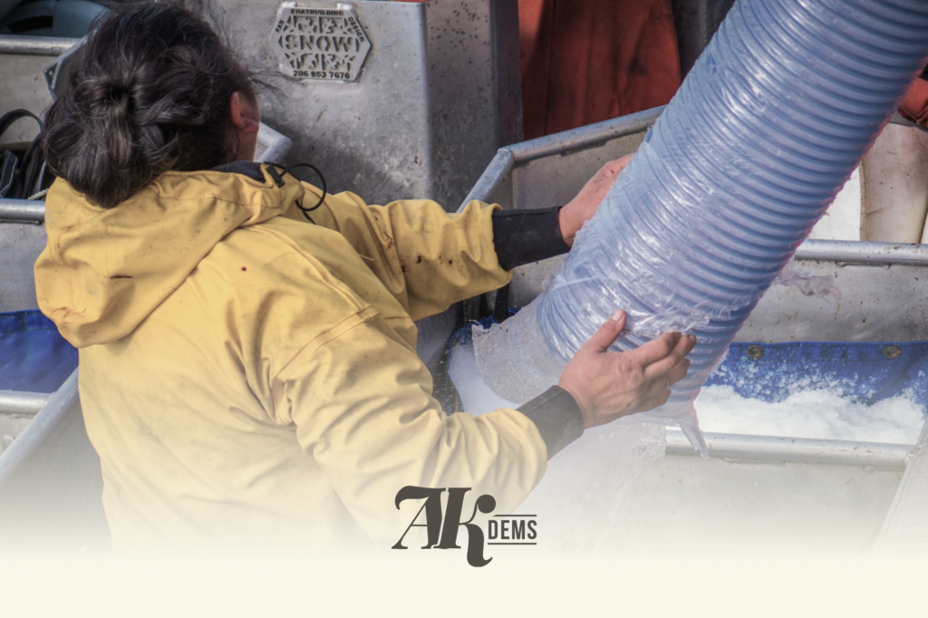 Worker in a yellow coverall grips a large blue flexible duct in an industrial setting.