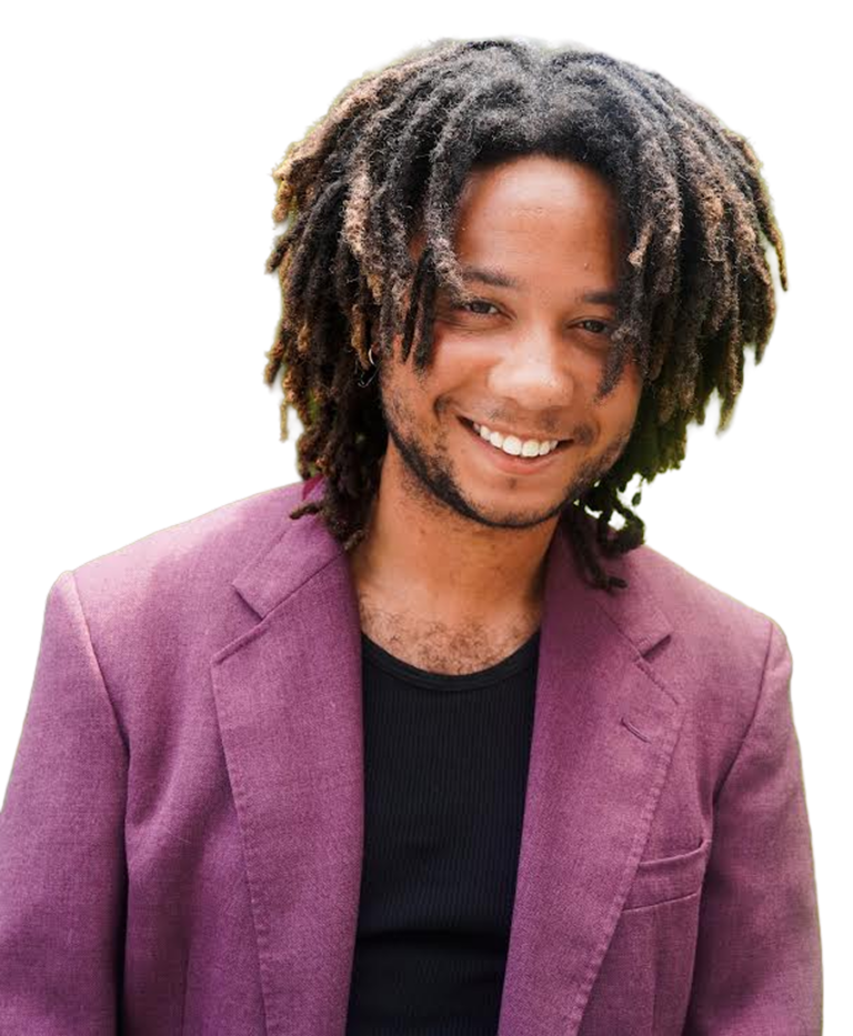 Portrait of a smiling man with dreadlocks wearing a pinkish-purple blazer and a black shirt.