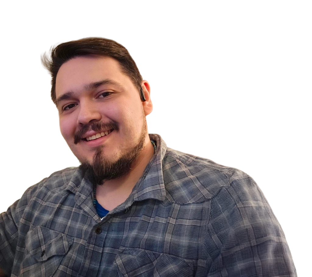 Smiling man with dark hair and a beard in a blue plaid shirt, angled selfie against a black background.